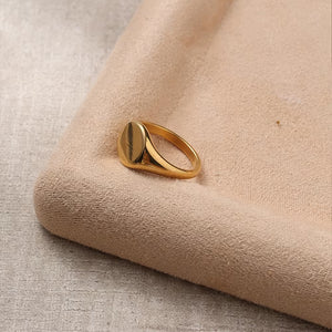 Gold-tone oval signet ring resting on pale fabric