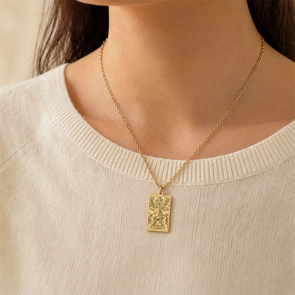 Gold Judgement tarot-card pendant necklace worn over a cream knit top.