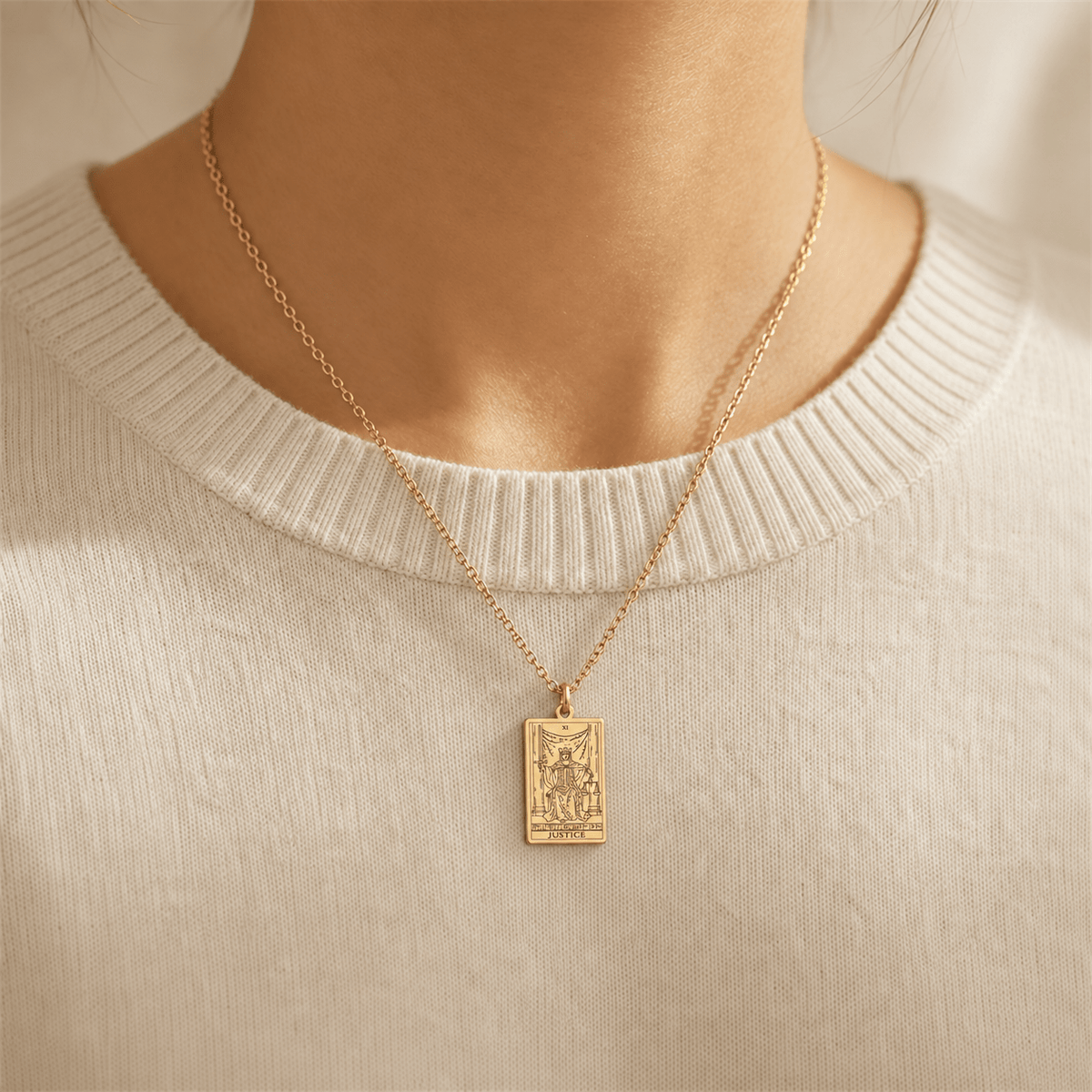 Gold-tone Justice tarot card necklace worn over a pale knit top