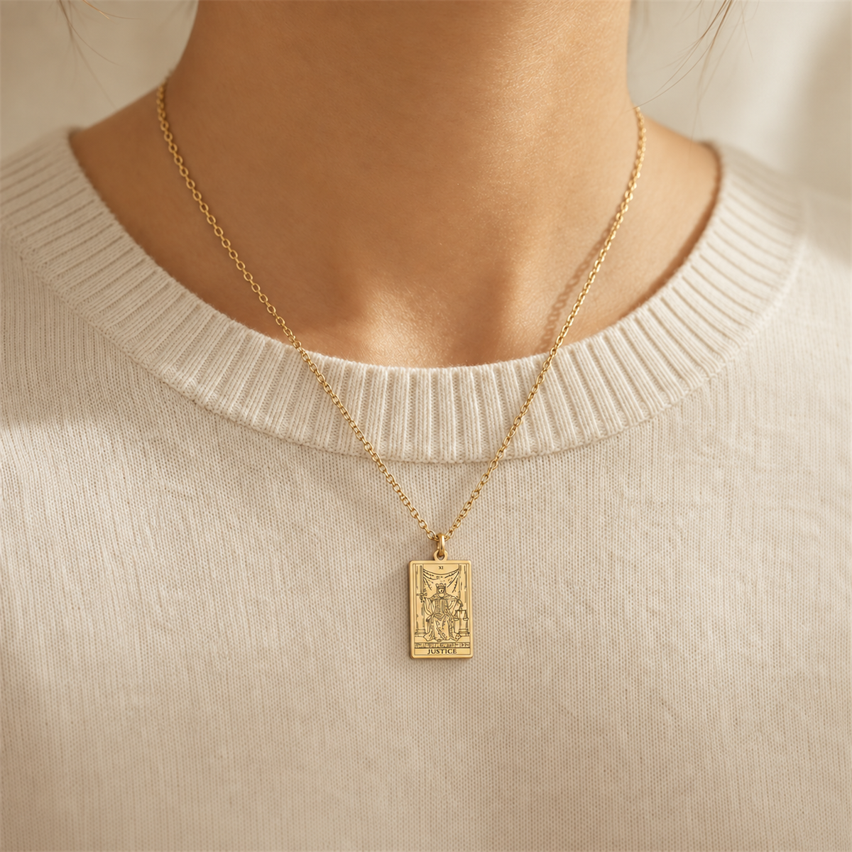 Gold Justice tarot-card pendant necklace worn over a cream knit top.