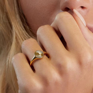 Gold-tone oval sunburst ring worn on a hand beside the face