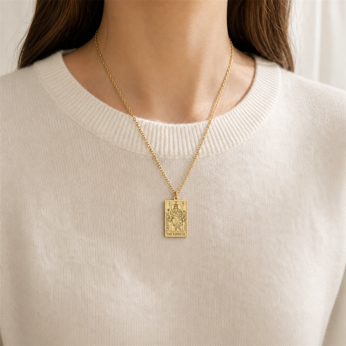 Gold The Emperor tarot-card pendant necklace worn over a cream knit top.
