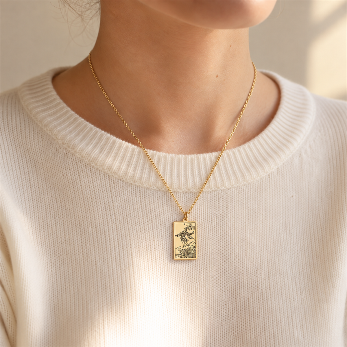 Gold The Fool tarot-card pendant necklace worn over a cream knit top.