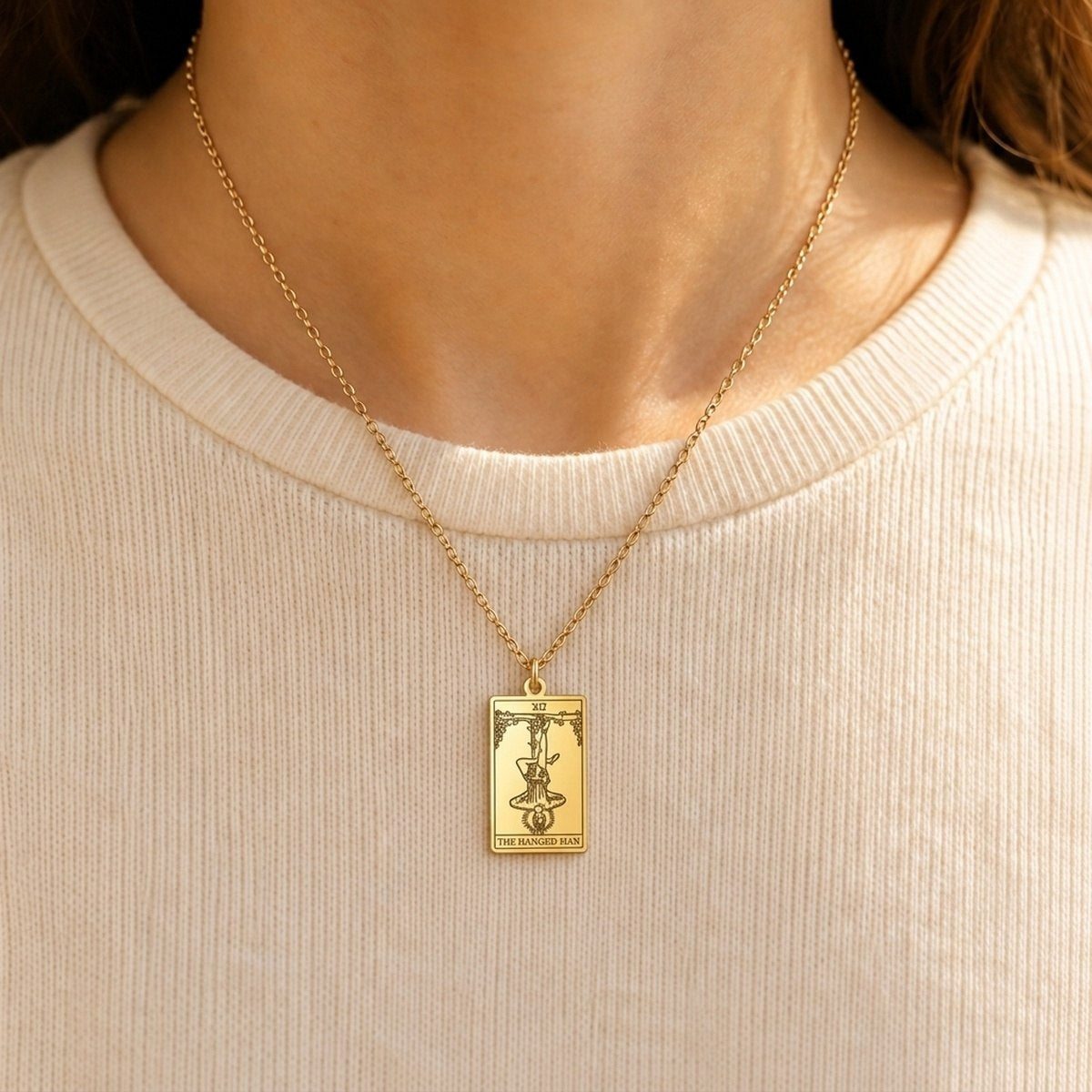 Gold The Hanged Man tarot-card pendant necklace worn over a cream knit top.