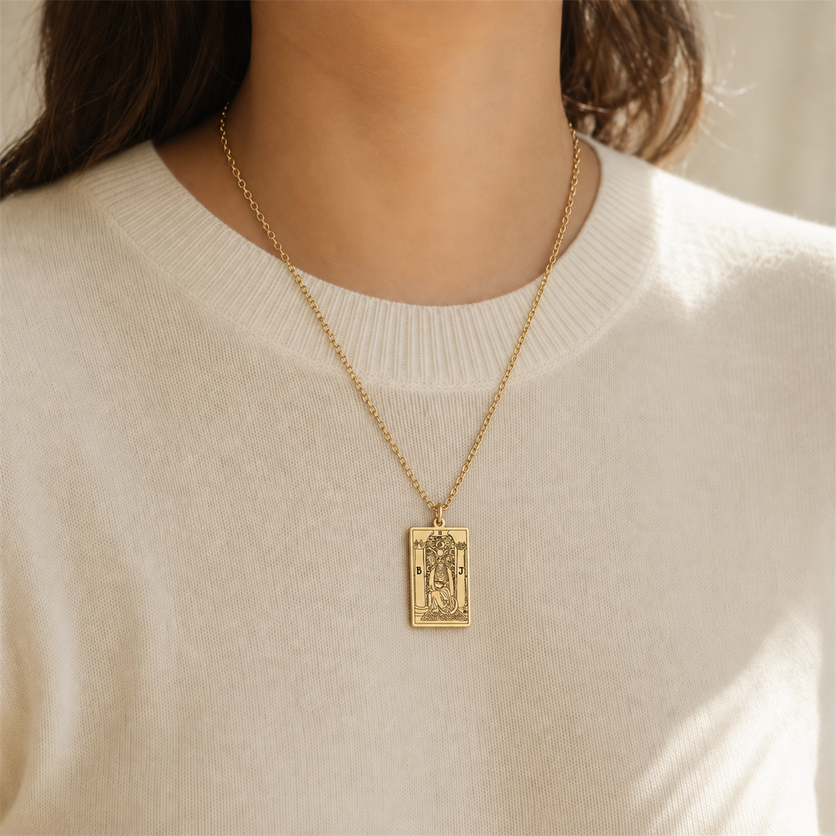 Gold The High Priestess tarot-card pendant necklace worn over a cream knit top.