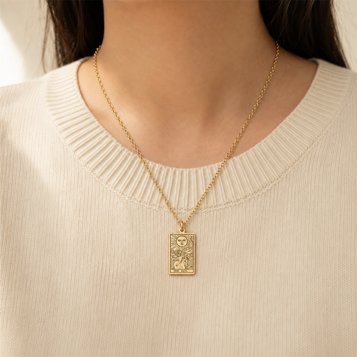 Gold The Sun tarot-card pendant necklace worn over a cream knit top.
