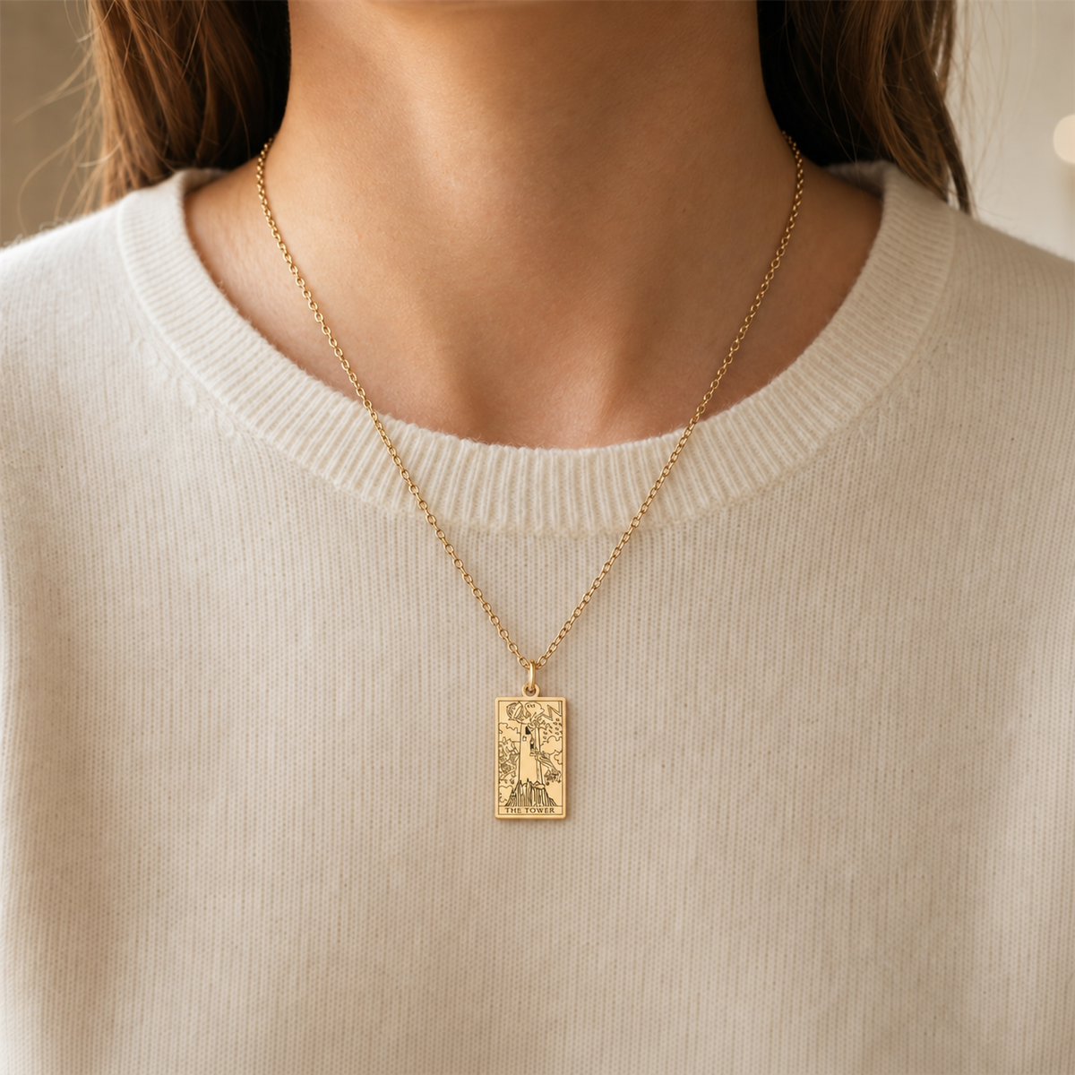 Gold The Tower tarot-card pendant necklace worn over a cream knit top.