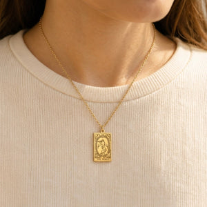 Gold The World tarot-card pendant necklace worn over a cream knit top.