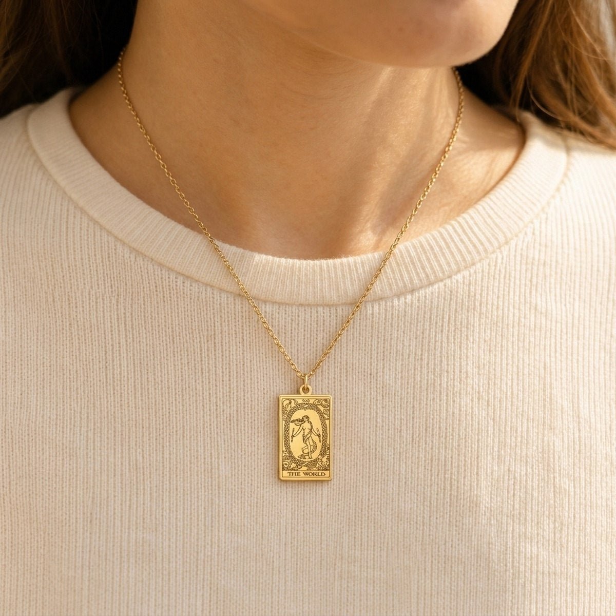 Gold-tone The World tarot card necklace worn over a pale knit top