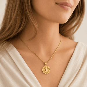 Model wearing a gold-tone compass-pattern pendant necklace with a pale neckline