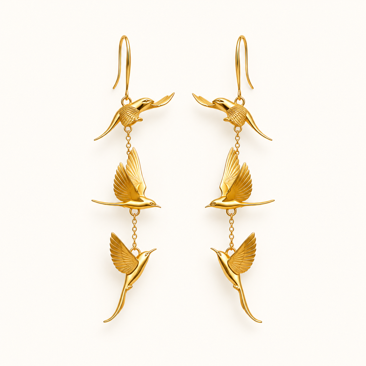 Gold-tone flying bird earrings on a warm-white background