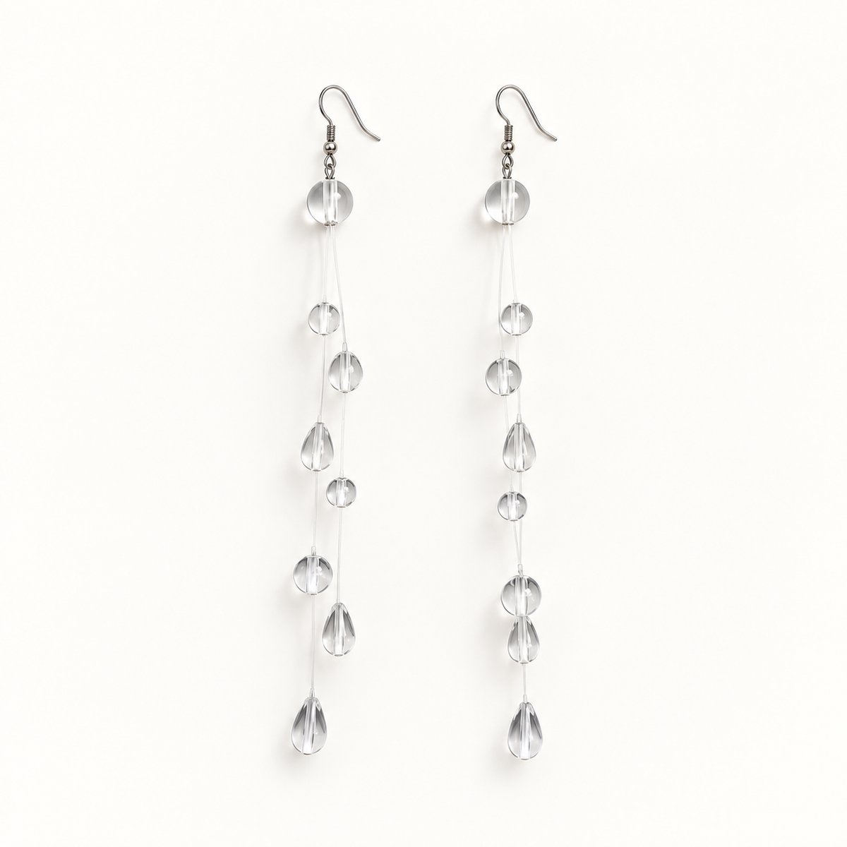 Silver-tone transparent drop earrings on a plain warm-white background