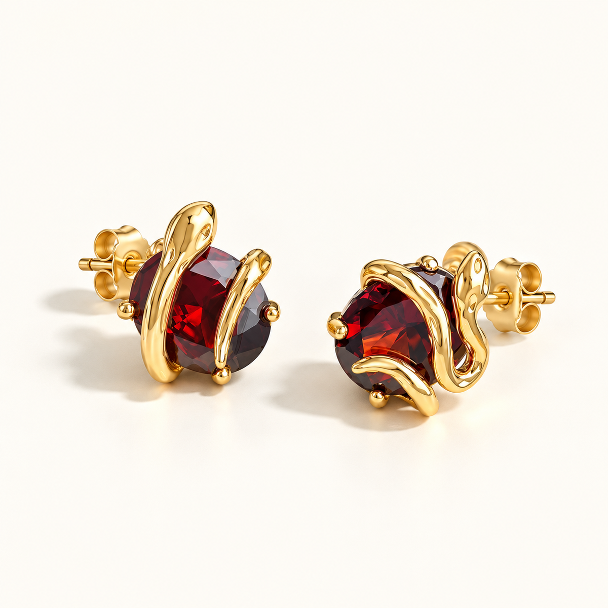 Gold-tone serpent stud earrings on a warm-white background