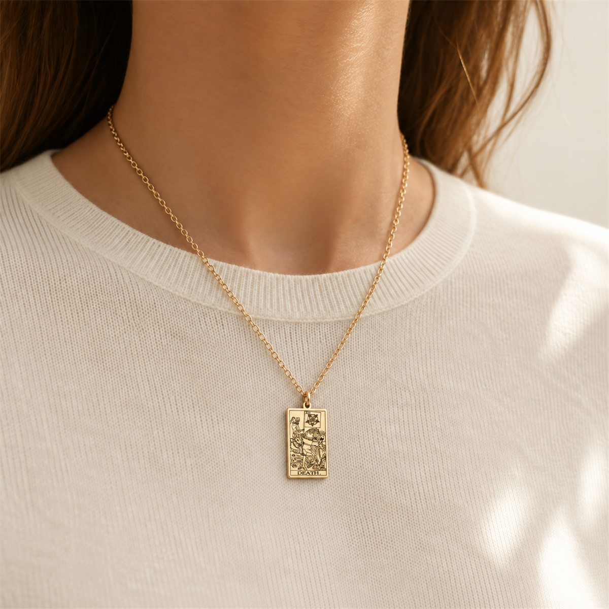 Gold Death tarot-card pendant necklace worn over a cream knit top.