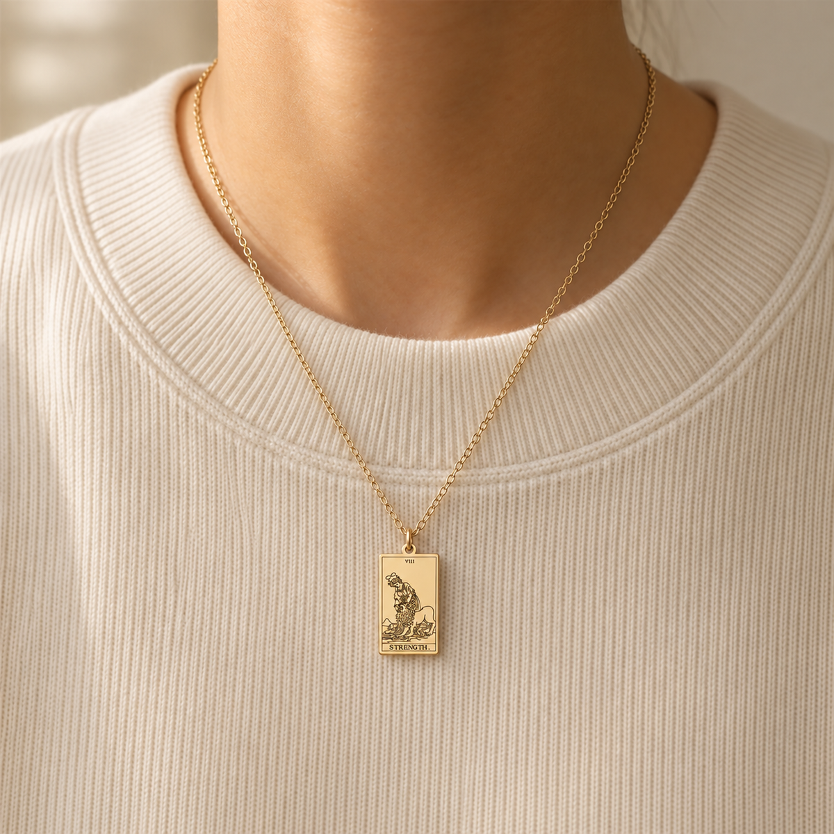 Gold Strength tarot-card pendant necklace worn over a cream knit top.
