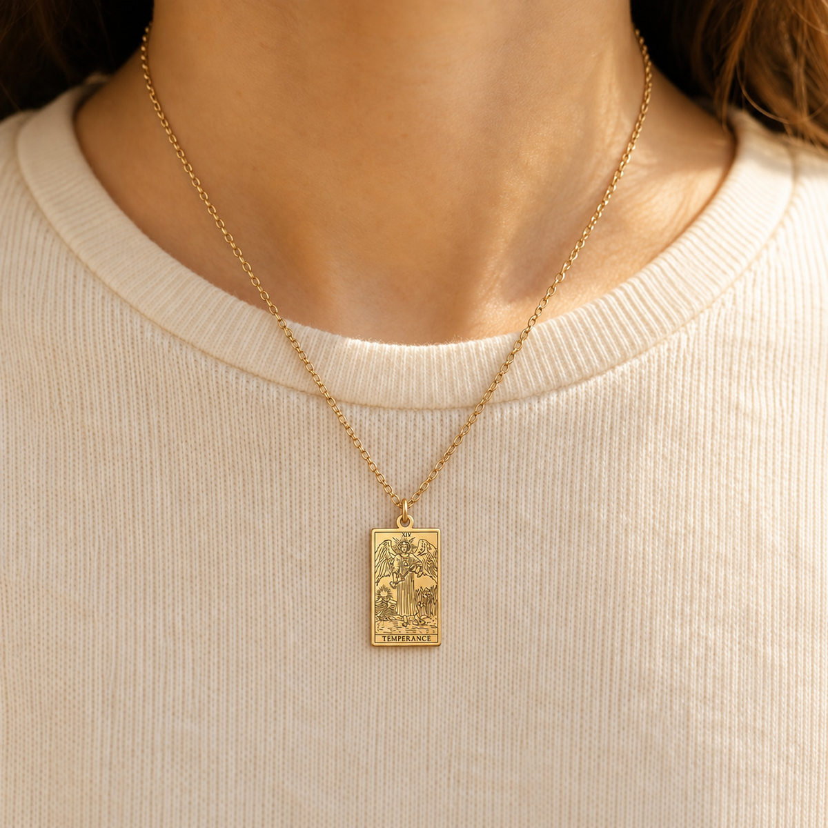 Gold Temperance tarot-card pendant necklace worn over a cream knit top.