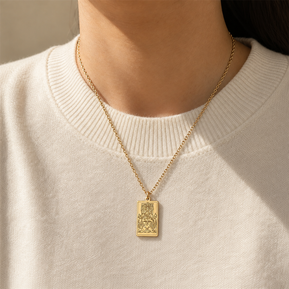 Gold The Chariot tarot-card pendant necklace worn over a cream knit top.