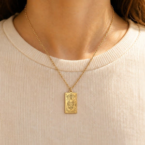 Gold The Devil tarot-card pendant necklace worn over a cream knit top.