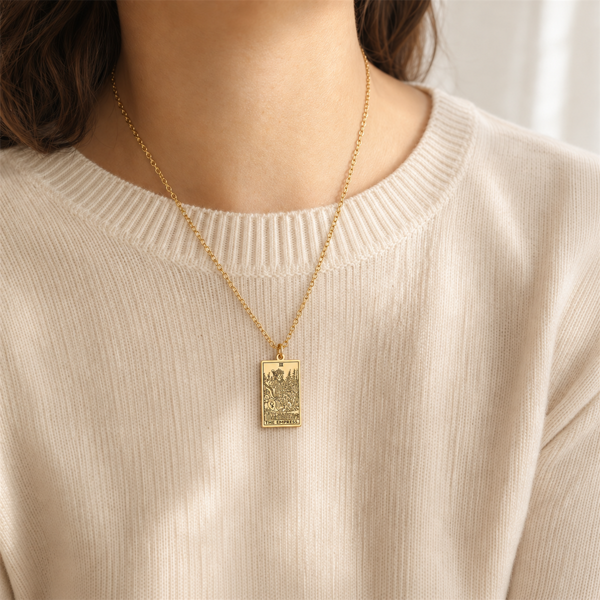 Gold The Empress tarot-card pendant necklace worn over a cream knit top.