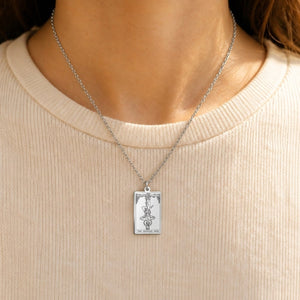 Silver The Hanged Man tarot-card pendant necklace worn over a cream knit top.