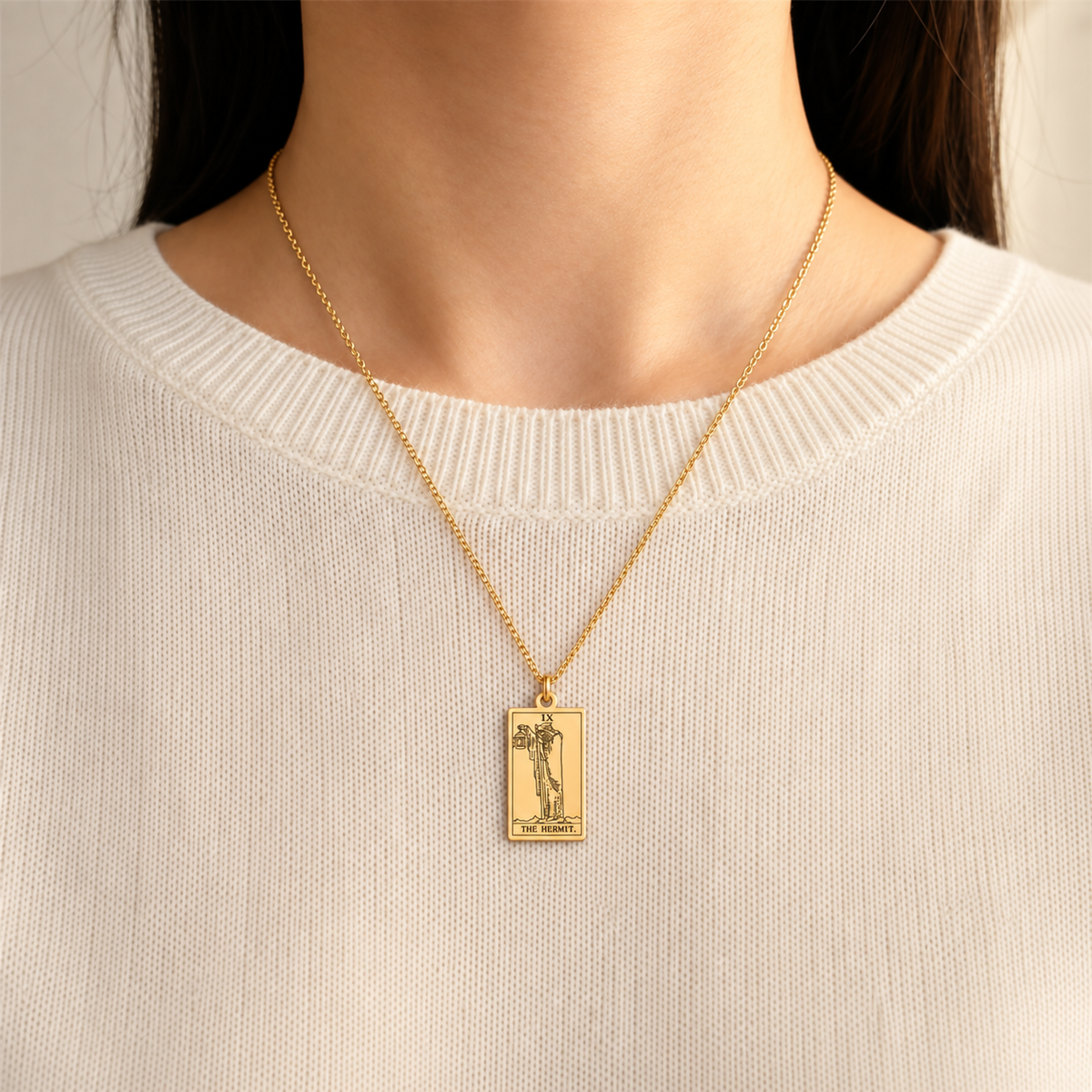 Gold The Hermit tarot-card pendant necklace worn over a cream knit top.