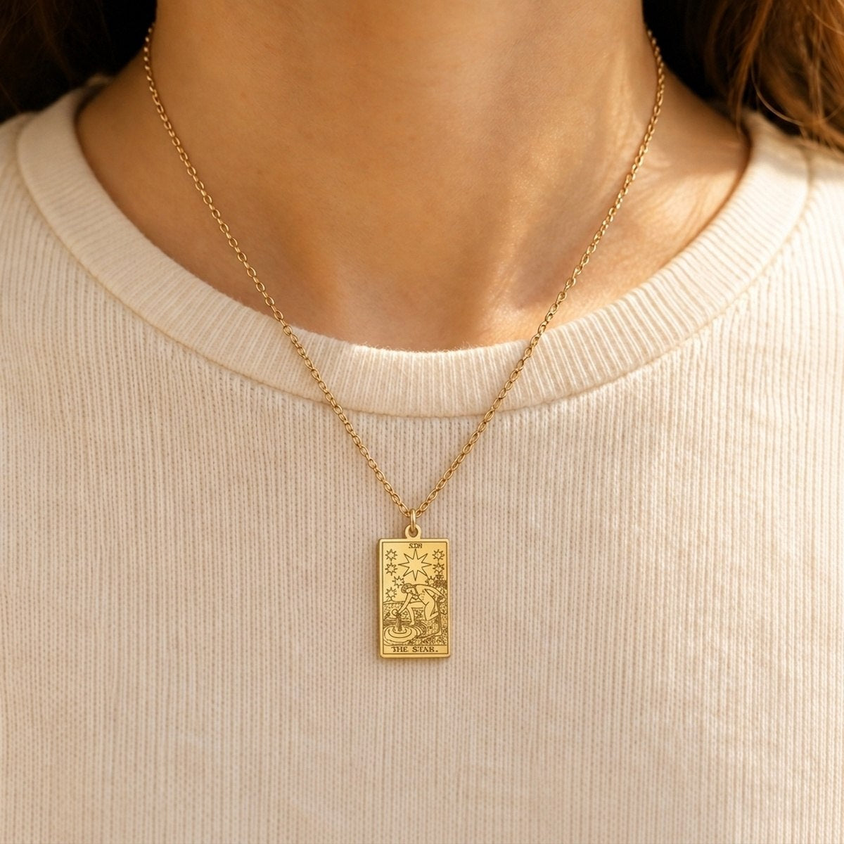 Gold The Star tarot-card pendant necklace worn over a cream knit top.