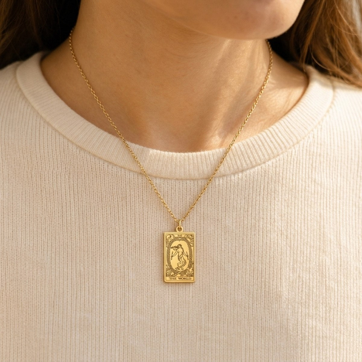 Gold The World tarot-card pendant necklace worn over a cream knit top.