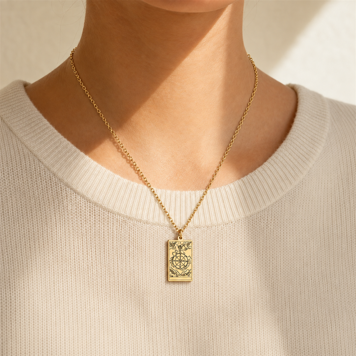 Gold Wheel of Fortune tarot-card pendant necklace worn over a cream knit top.